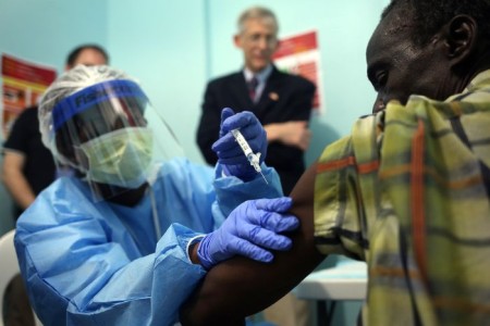 MONROVIA, LIBERIA - FEBRUARY 02: A nurse administers an injection on the first day of the Ebola vaccine study being conducted at Redemption Hospital, formerly an Ebola holding center, on February 2, 2015 in Monrovia, Liberia. Twelve people were given injections Monday, out of a planned 27,000 people in the Monrovia area. The clinical research study is being conducted jointly by the U.S. National Institutes of Health (NIH), and the Liberian Ministry of Health. The Ebola epidemic virus has killed at least 3,700 people in Liberia alone, the most of any country, and nearly 9,000 across in West Africa. In background of photo is Dr. Clifford Lane, Clinical Director of the U.S. National Institute for Allergy and Infectious Diseases. (Photo by John Moore/Getty Images)