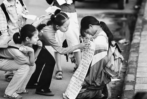 Двое девочек читают надпись на плакате девочки, просящей милостыню на улице. Фото: Великая Эпоха.