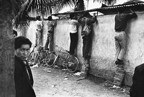 Приезжие в провинцию Хайнань из других провинций, у кого нет специальных пропусков, были схвачены, а те, кому посчастливилось убежать, заглядывают через забор и смотрят как там их родственники и друзья. Провинция Хайнань. 1992 год. Фото: Huan Yiming