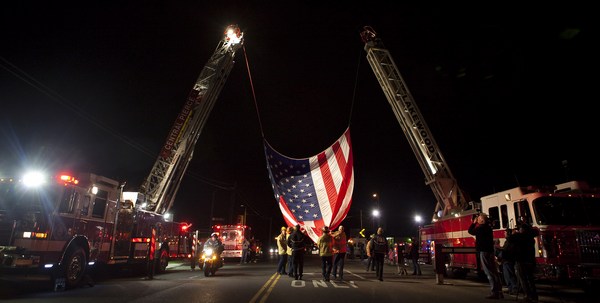 Пожарные поднимают гигантский флаг на автокране, чтобы чтить память четырех Лейквудских полицейских. Фото: Stephen Brashear/Getty Images)