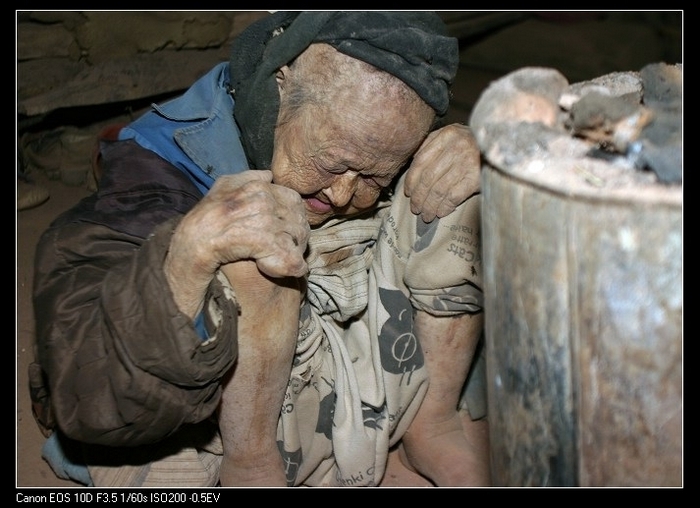 У бабушки Ван, которой уже за 80 лет, нет денег на лечение. Она часто подолгу сидит так, прислонившись к тёплой печи, чтобы хоть немного ослабить свои страдания. Провинция Гуйчжоу. Фото с epochtimes.com