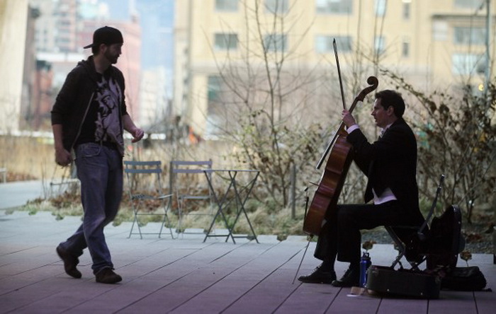 Прохожий подходит к уличному музыканту в парке Хай-Лайн, Нью-Йорк, чтобы отблагодарить его деньгами. Фото: Mario Tama/Getty Images