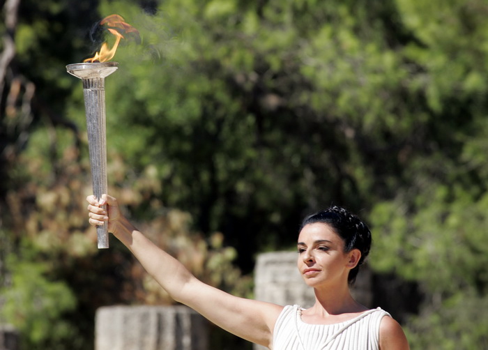 Театрализованное представление заключается в том, что 11 женщин в греческих костюмах сопровождают факел, который зажигает от солнца одна из них — жрица Протиериа. Затем она передаёт его первому спортсмену-факелоносцу. Фото: Milos Bicanski/Getty Images