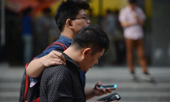Двое мужчин используют свои мобильные устройства на улице в Шанхае 25 сентября 2013 года. Чиновники и государственные служащие, работающие в правительственных ведомствах и в офисах Коммунистической партии в Шанхае, устремились за покупкой сотовых телефонов с шифрованием, в то время как проводится антикоррупционная проверка. в Шанхае. (Питер Паркс / AFP / Getty Images) | Epoch Times Россия