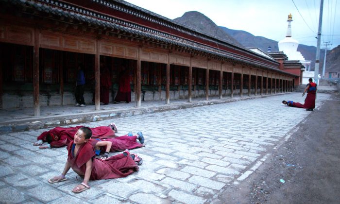 Молодой монах (слева) простирается ниц возле монастыря Лабранг в Сяхэ, провинция Ганьсу, который стал горячей точкой многих тибетских протестов против китайских властей 16 мая 2013 года. С 2009 года более 13o тибетцев подожгли себя, большинство из них умерло от полученных травм, в демонстрациях против того, что они считают китайским угнетением. Пекин отвергает такие утверждения, указывая на значительные инвестиции в Тибет и другие регионы с большим тибетским населением, хотя критики говорят, что экономическое развитие привело к притоку этнических ханьских китайцев и подорвало традиционную тибетскую культуру. (Эд Джонс / AFP / Getty Images) | Epoch Times Россия