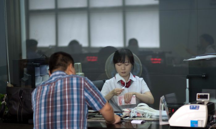 Сотрудник отделения Промышленно-коммерческого банка China Ltd (ICBC) считает деньги, обслуживая клиента в Шанхае 24 сентября 2014 г. (JOHANNES EISELE / AFP / Getty Images) | Epoch Times Россия