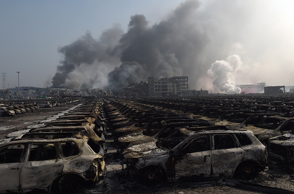На фоне дыма стоят ряды выгоревших автомобилей Volkswagen. 13 августа 2015 года в портовом городе Тяньцзине, на севере Китая,  раздалось несколько мощных взрывов. Государственные СМИ сообщили о 17 погибших. Фото: GREG BAKER/AFP/Getty Images | Epoch Times Россия