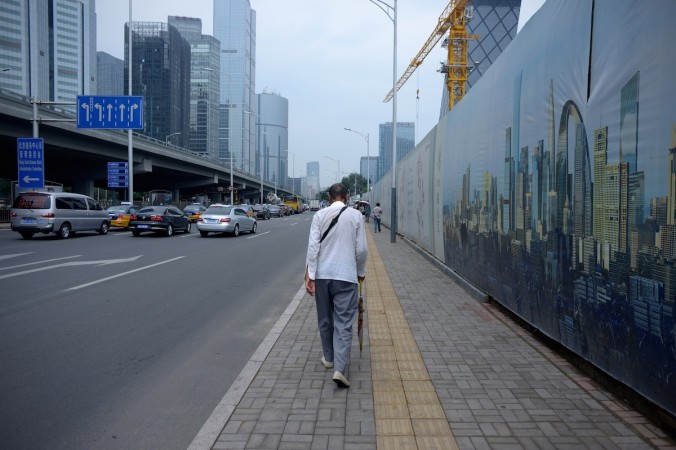 Человек проходит мимо строительной площадки в Пекине 28 июля 2015 года. В последние годы Китай использует грандиозные, но бесполезные проекты для стимуляции роста ВВП. Фото: WANG ZHAO/AFP/Getty Images | Epoch Times Россия