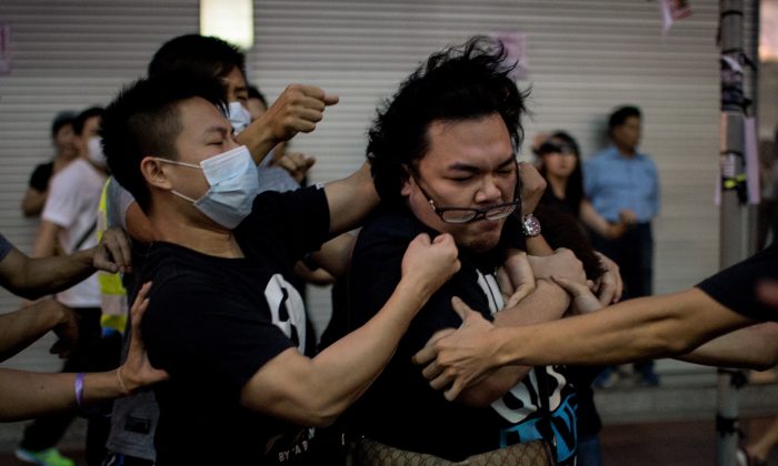 Группа мужчин в масках избила мужчину (справа), который пытался помешать им сносить баррикады в зоне протестов за демократию в районе Козуэй-Бэй в Гонконге 3 октября 2014 года. Источники сообщают, что главный исполнительный директор Гонконга Люн Чунь-ин использовал мафиозные группы для преследования протестующих. (Алекс Огл / AFP / Getty Images) | Epoch Times Россия