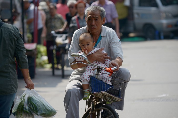 Пожилой человек едет с младенцем на велосипеде по Пекину, 8 сентября 2015 года. Фото: Wang Zhao/AFP/Getty Images | Epoch Times Россия
