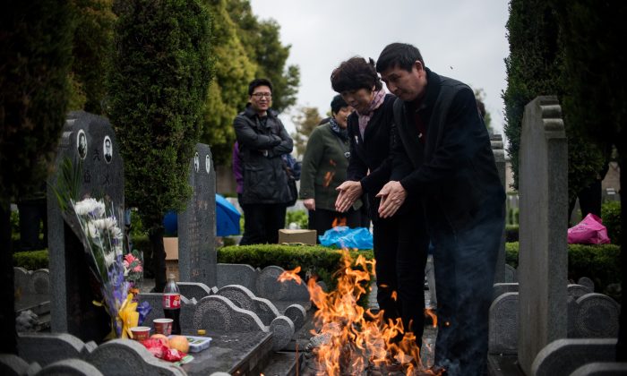 Пара молится, сжигая бумажные деньги во время ежегодного фестиваля «Цинмин», или Дня чистки гробниц, на общественном кладбище в Шанхае 6 апреля 2015 г. (Johannes Eisele / AFP / Getty Images) | Epoch Times Россия