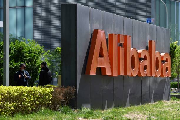 Двое сотрудников Alibaba беседуют за вывеской Alibaba возле офиса компании в Пекине, 13 апреля 2021 года.. Фото: GREG BAKER/AFP via Getty Images | Epoch Times Россия