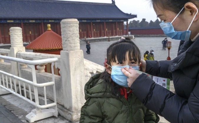 Мама надевает защитную маску на лицо дочери в  Храме Неба в Пекине, Китай, 27 января 2020 года. Kevin Frayer/Getty Images | Epoch Times Россия
