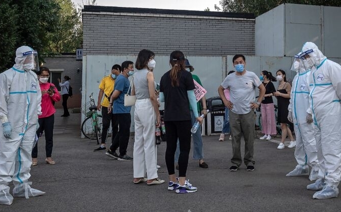 Сотрудники, одетые в средства индивидуальной защиты, возле группы людей в масках, ожидающих  тестирования на COVID-19 в Пекине 19 июня 2020 года. NICOLAS ASFOURI/AFP via Getty Images | Epoch Times Россия