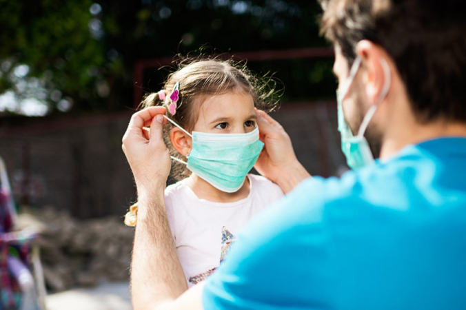 Взрослый надевает медицинскую маску девочке. SanyaSM/E+/Getty Images | Epoch Times Россия