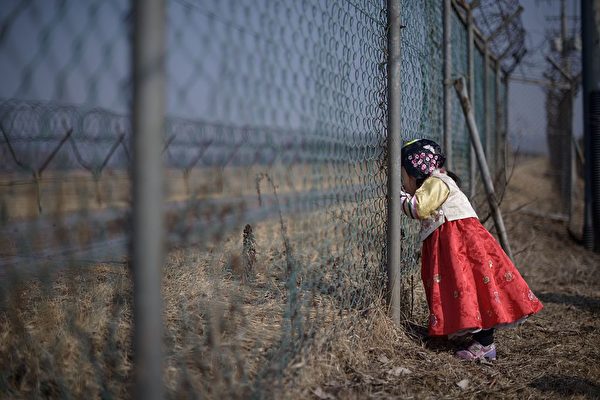 Девочка в традиционном платье ханбок стоит у военного забора, обращеённого в сторону Северной Кореи, в парке Имджингак, к югу от военной демаркационной линии и демилитаризованной зоны (ДМЗ), разделяющей Северную и Южную Корею, 19 февраля 2015 года. ED JONES/AFP/Getty Images | Epoch Times Россия