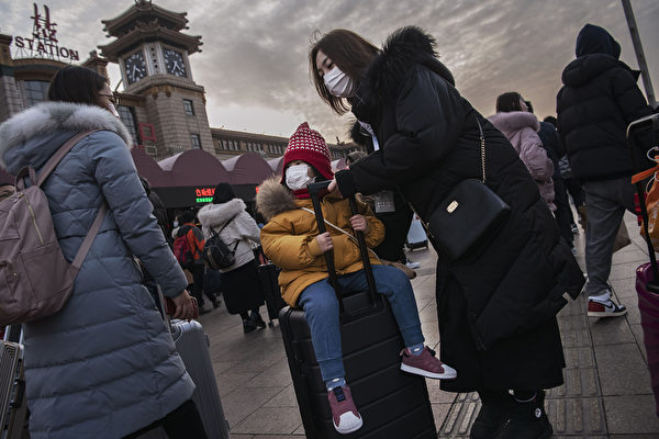 Мать везёт чемодан, на котором сидит девочка в защитной маске, чтобы сесть на поезд на железнодорожном вокзале Пекина перед ежегодным праздником весны, Пекин, Китай 21 января 2020 года. Kevin Frayer/Getty Images | Epoch Times Россия