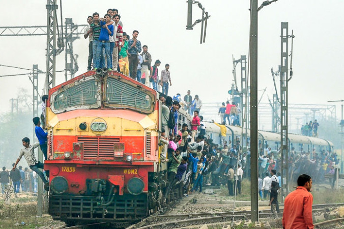 Индийские пассажиры стоят и висят на поезде, когда он отходит от станции на окраине Нью-Дели. Фото: MONEY SHARMA/AFP/Getty Images | Epoch Times Россия