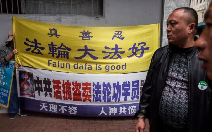 Последователь Фалуньгун (слева) держит транспаранты и табличку, рядом мужчины из туристической группы материкового Китая, Коулун, Гонконг, 6 января 2019 г. (Isaac Lawrence/AFP via Getty Images) | Epoch Times Россия