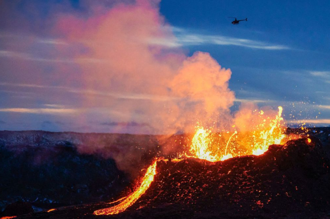 Вертолёт пролетает над лавой, вытекающей из трещины вулкана Фаградальсфьядль на полуострове Рейкьянес в Исландии, примерно в 40 километрах от Рейкьявика, 6 апреля 2021 года. HALLDOR KOLBEINS / AFP via Getty Images | Epoch Times Россия
