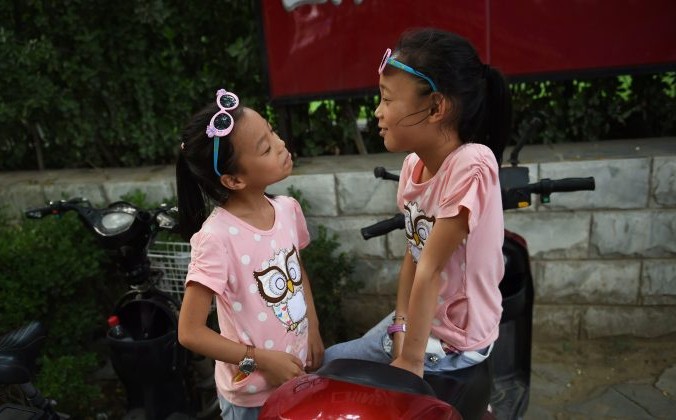 Две сестры играют на электросамокате своих родителей в Пекине 10 июля 2015 года. Политика одного ребёнка проводится уже более трёх десятилетий, но, столкнувшись с последствиями сокращения рабочей силы и быстро стареющего населения, Пекин начинает ослаблять ограничения последних лет и поощряет рождение большего числа детей. Фото: GREG BAKER/AFP/Getty Images | Epoch Times Россия
