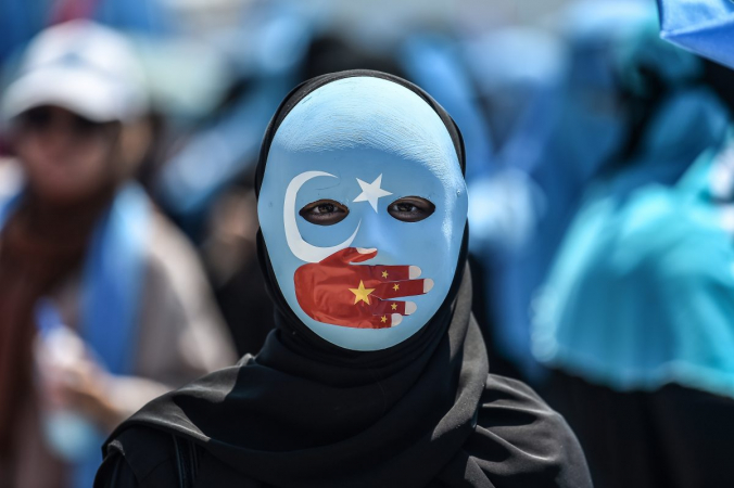 Демонстрант в маске, раскрашенной в цвета флага Синьцзяна, принимает участие в акции протеста, осуждающей обращение Китая с этническими мусульманами-уйгурами, перед китайским консульством в Стамбуле 5 июля 2018 года. (OZAN KOSE/AFP/Getty Images) | Epoch Times Россия