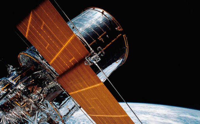 Гигантский космический телескоп «Хаббл» подвешен в космосе с помощью системы удалённого манипулятора (RMS) Discovery после развёртывания части его солнечных панелей и антенн 25 апреля 1990 г. NASA via AP | Epoch Times Россия