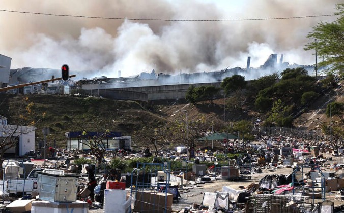 На заднем плане горит фабрика, а на переднем — пустые коробки от вывозимых разграбленных товаров на окраине Дурбана, ЮАР, 14 июля 2021 года. AP Photo | Epoch Times Россия