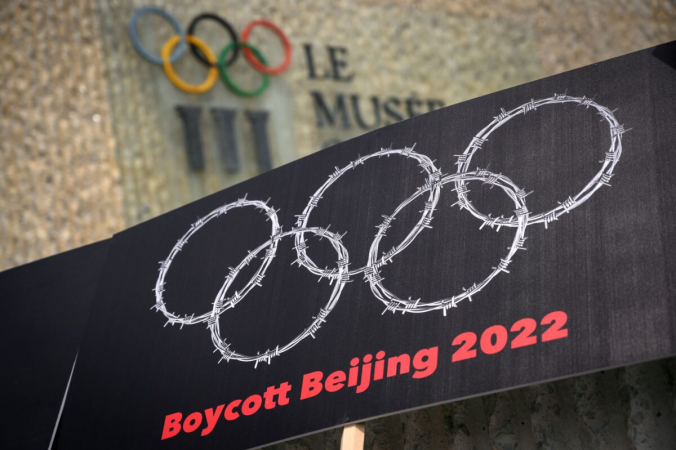Плакат с колючей проволокой в форме олимпийских колец рядом с вывеской Олимпийского музея во время акции протеста, организованной тибетскими и уйгурскими активистами против зимних Олимпийских игр 2022 года в Пекине. Лозанна, Швейцария, 23 июня 2021 года. (Fabrice Coffrini/AFP via Getty Images) | Epoch Times Россия