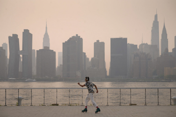Мужчина катается на коньках перед задымлённым горизонтом Манхэттена в парке в Бруклинском районе Нью-Йорка 20 июля 2021 года. ED JONES/AFP via Getty Images | Epoch Times Россия