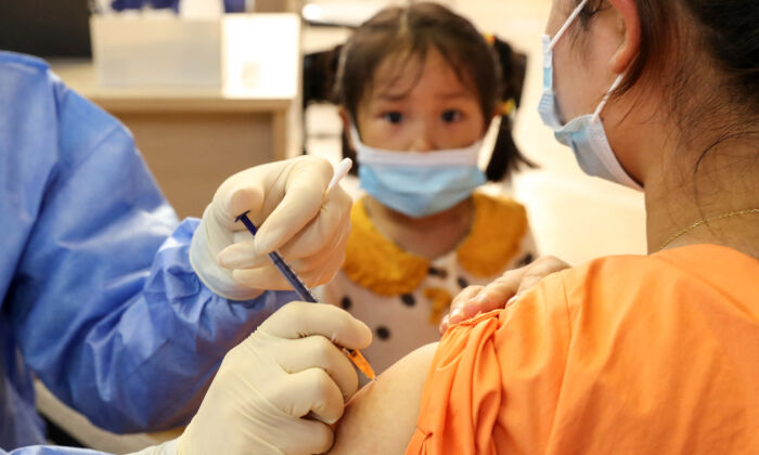 Ребёнок наблюдает, как женщина получает вакцину COVID-19 Китайской национальной биотехнологической группы (CNBG) в Наньтуне, в восточной провинции Китая Цзянсу, 5 июля 2021 г. (STR / AFP через Getty Images) | Epoch Times Россия