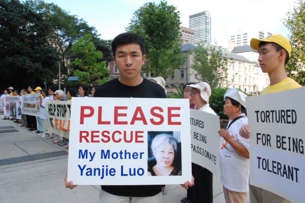 Фань Вента держит табличку с портретом своей матери Ло Яньцзе, которая в 2011 году была приговорена к 13 годам тюремного заключения в Китае за практику Фалуньгун, возле мэрии Торонто 25 августа 2016 года. (Yi Ling/Epoch Times)