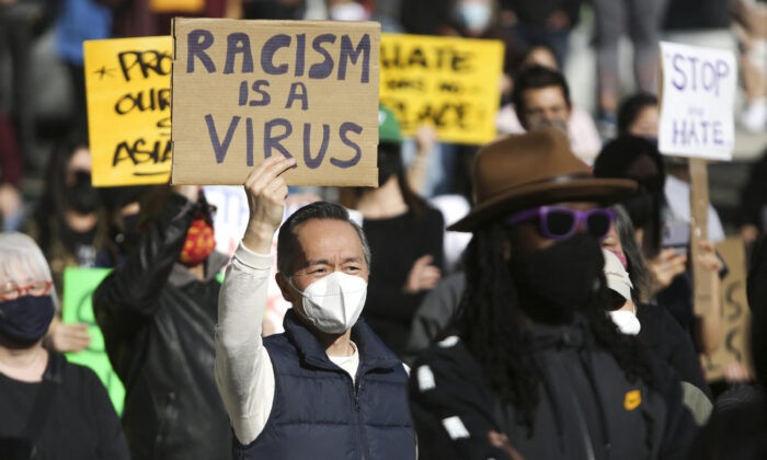 Мужчина держит табличку «Расизм — это вирус» во время митинга «Мы не молчим» в ответ на недавнее преступление в китайском квартале Сиэтла, штат Вашингтон, 13 марта 2021 года. (Джейсон Редмонд / AFP через Getty Images) | Epoch Times Россия