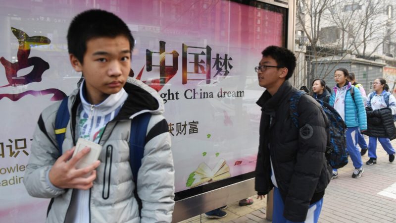 Молодые люди проходят мимо пропагандистского рекламного щита о «Китайской мечте», лозунга, связанного с китайским лидером Си Цзиньпином, возле школы в Пекине 12 марта 2018 года. (Greg Baker/AFP via Getty Images) | Epoch Times Россия