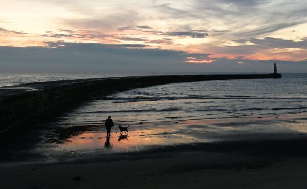 Мужчина выгуливает собаку вдоль пляжа на восходе солнца в гавани Сихем, город Сихем, северо-восточная Англия, 7 октября 2021 года. (Paul Ellis/AFP via Getty Images)