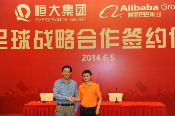 Основатель и председатель совета директоров Alibaba Group Джек Ма (справа) пожимает руку председателю Evergrande Group Сюй Цзяиню во время церемонии подписания соглашения между Alibaba Group и Evergrande Group о покупке Alibaba 50% акций Guangzhou Evergrande 5 июня 2014 года в Гуанчжоу, провинция Гуандун, Китай. (VCG/VCG via Getty Images)