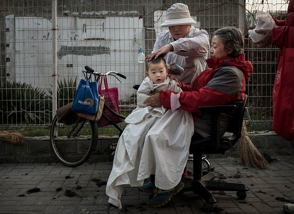 Китайский парикмахер стрижёт ребёнка на улице 28 ноября 2014 года в Пекине, Китай. Хотя Китай имеет одну из самых быстрорастущих экономик в мире, неравенство доходов по-прежнему является серьёзной проблемой, поскольку значительная часть населения страны живёт ниже национального уровня бедности. (Kevin Frayer/Getty Images)