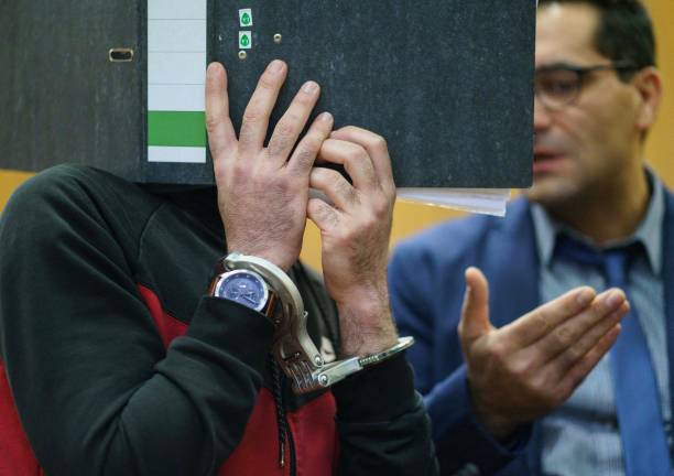 Обвиняемый закрывает лицо от камер. Фото: FRANK RUMPENHORST/POOL/AFP via Getty Images) | Epoch Times Россия