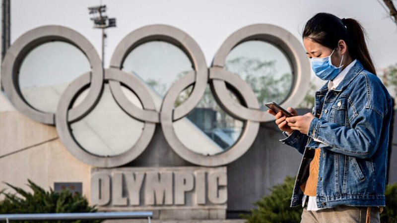 Женщина в маске идёт перед скульптурой олимпийских колец на национальном стадионе «Птичье гнездо» в Пекине 23 марта 2020 года. (Nicolas Asfouri/AFP via Getty Images) | Epoch Times Россия
