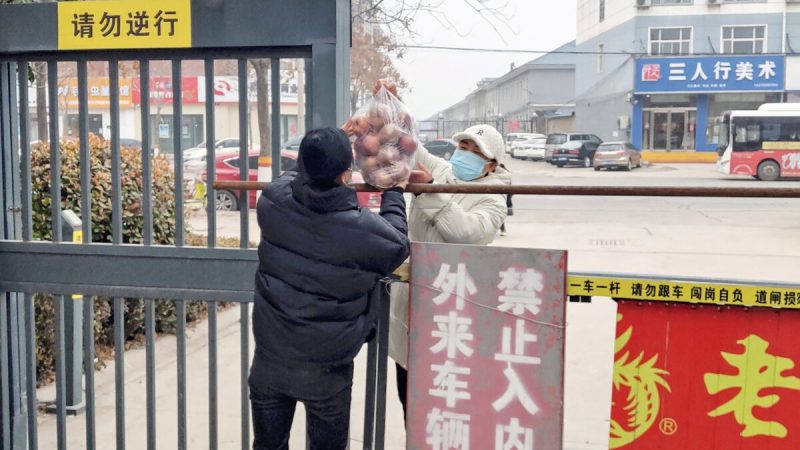 Житель получает еду у входа в жилую зону, закрытую и ограниченную из-за вспышки КОВИД-19 в Аньяне, провинция Хэнань, 12 января 2022 года. (STR/AFP via Getty Images) | Epoch Times Россия