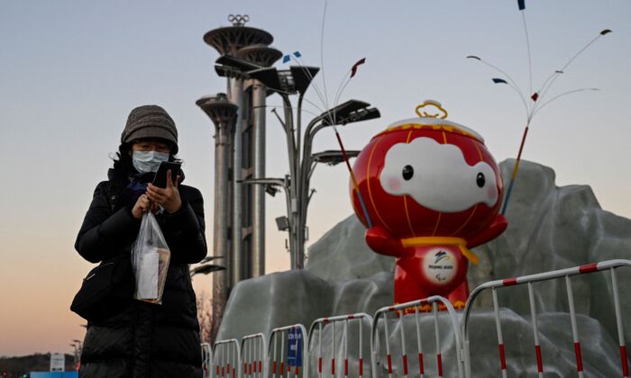 Женщина проверяет свой телефон перед инсталляцией Шуи Рон Рон, талисмана зимних Паралимпийских игр 2022 года в Олимпийском парке в Пекине 13 января 2022 года. Фото: Jade Gao/AFP / Getty Images | Epoch Times Россия