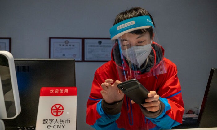 Сотрудник на стойке регистрации отеля Prince Ski Town проверяет телефон за табличкой с надписью «цифровые юани (e-CNY) принимаются» в Чжанцзякоу, Китай, 4 декабря 2021 г. (Andrea Verdelli/Getty Images) | Epoch Times Россия
