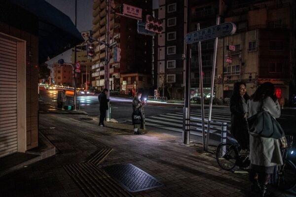 Люди идут по улице жилого района во время отключения электричества в районе Кото в Токио рано утром 17 марта 2022 года после мощного землетрясения магнитудой 7,4, потрясшего восточную часть Японии. (Philip Fong/AFP via Getty Images)