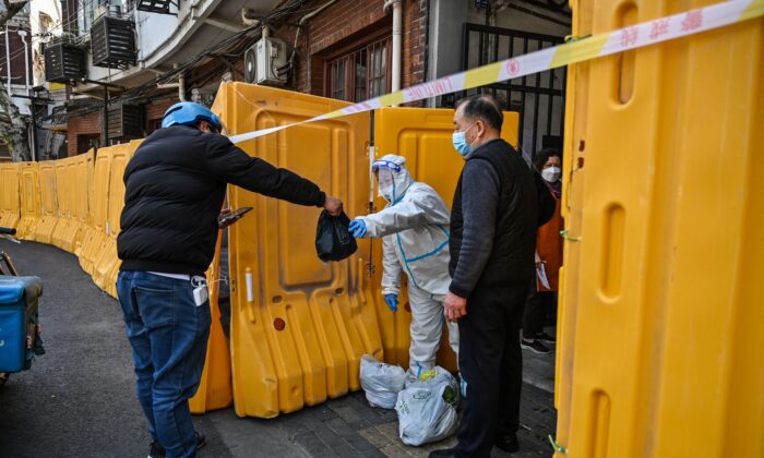 Рабочий в защитном снаряжении охраняет вход в закрытый район в качестве меры против коронавируса Covid-19 и получает еду от курьера в районе Цзинъань в Шанхае, 29 марта 2022 года. Фото: HectorRetamal/AFP viaGettyImages
 | Epoch Times Россия