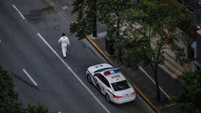 Рабочий, одетый в средства индивидуальной защиты, идёт рядом с полицейской машиной во время блокировки COVID-19 в районе Цзинъань в Шанхае 11 апреля 2022 года. (HECTOR RETAMAL/AFP via Getty Images)  | Epoch Times Россия