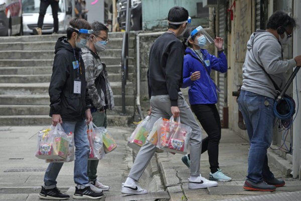 Рабочие раздают людям пакеты с материалами для профилактики коронавируса во время противоэпидемического мероприятия в Гонконге, 2 апреля 2022 года. Фото: Kin Cheung/AP Photo