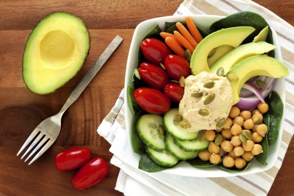 Продуктовая тарелка для здорового обеда с авокадо, хумусом и свежими овощами.
