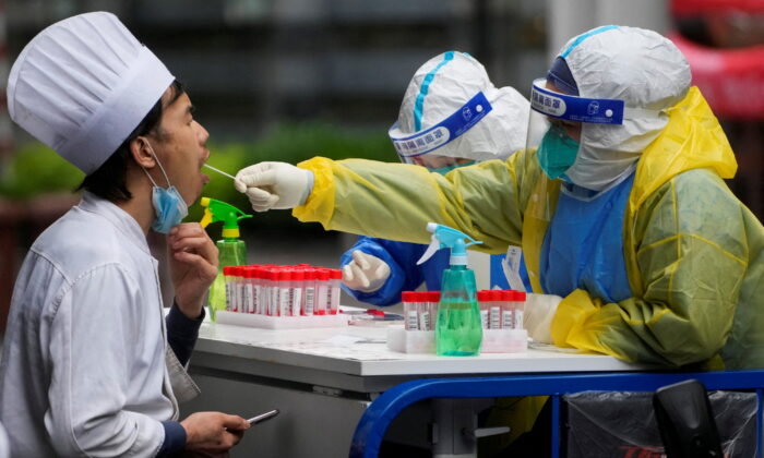 Медицинский работник в защитном костюме берёт образец мазка у кухонного работника для анализа на нуклеиновые кислоты во время блокировки COVID-19 в Шанхае, Китай, 13 мая 2022 года. (Aly Song/Reuters) | Epoch Times Россия
