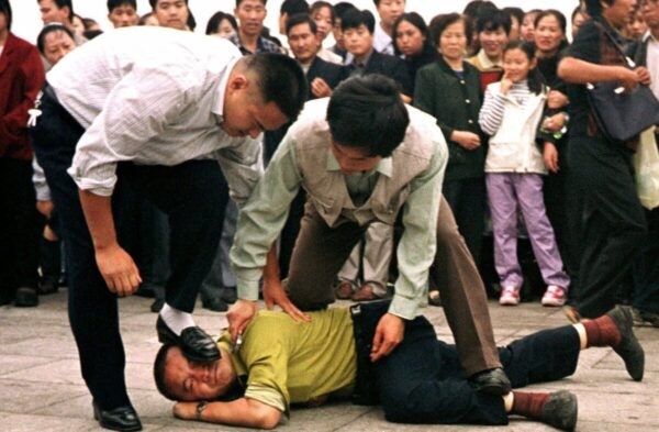 Полиция задерживает последователя Фалуньгун на площади Тяньаньмэнь, толпа наблюдает за происходящим в Пекине 1 октября 2000 года. (AP Photo/Chien-min Chung)