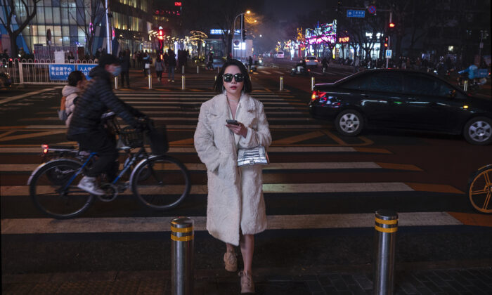Женщина переходит дорогу на светофоре в элитном торговом районе в туманный вечер в Пекине, Китай, 24 марта 2022 года. (Kevin Frayer/Getty Images) | Epoch Times Россия